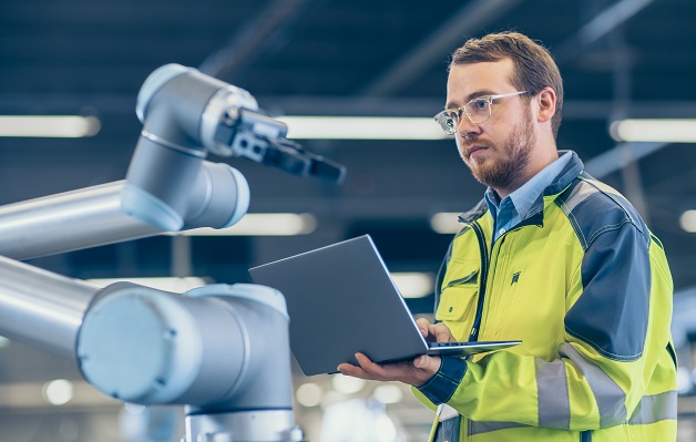 Automation engineer uses laptop for programming robotic arm